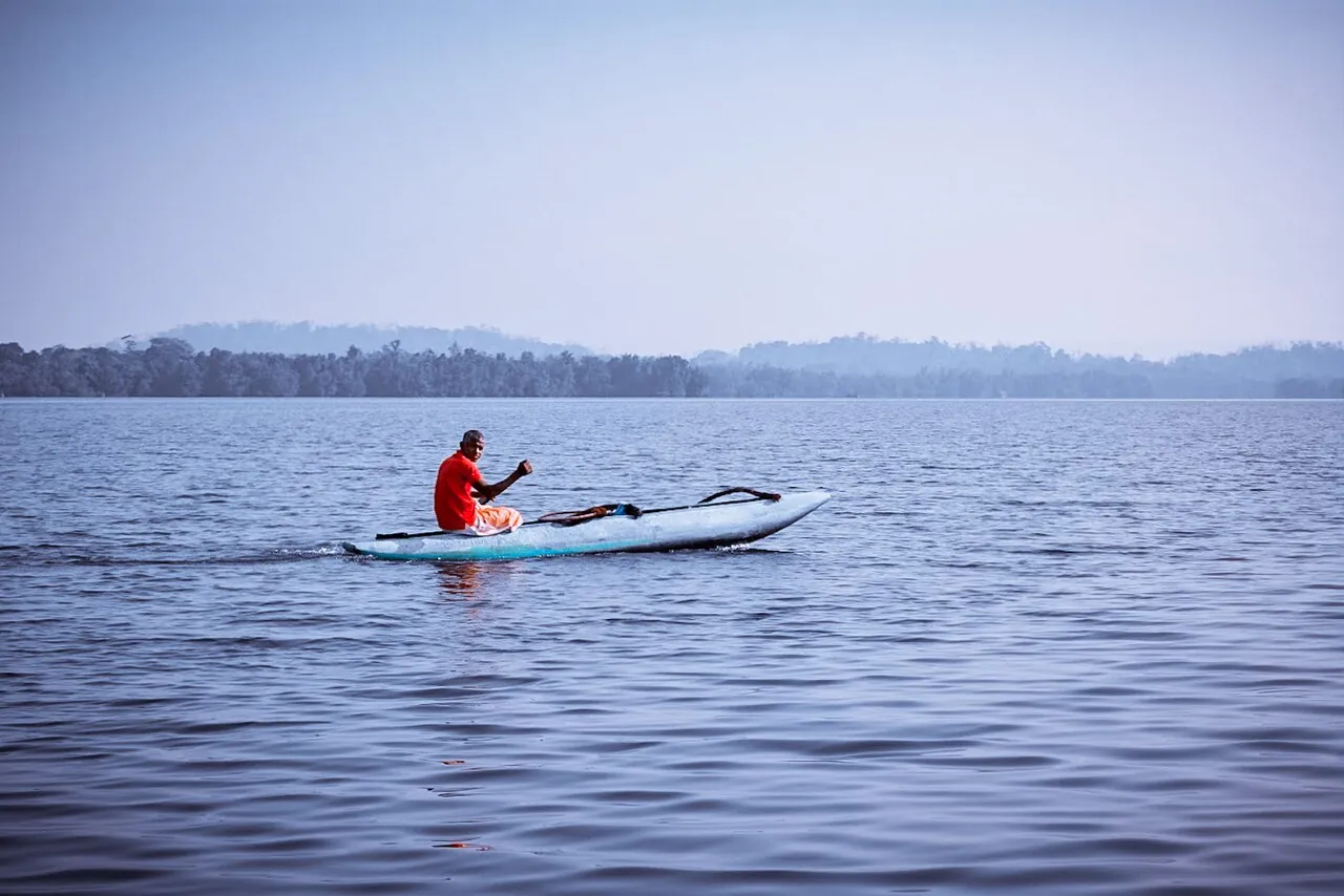 A fisherman paddling across open Madu River water